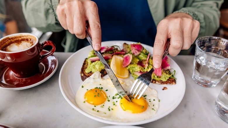 Person äter ägg och avokadomacka med kaffe och vatten på restaurang